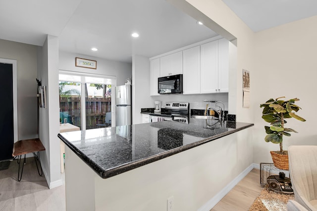 kitchen with kitchen peninsula, appliances with stainless steel finishes, dark stone counters, light hardwood / wood-style flooring, and white cabinetry