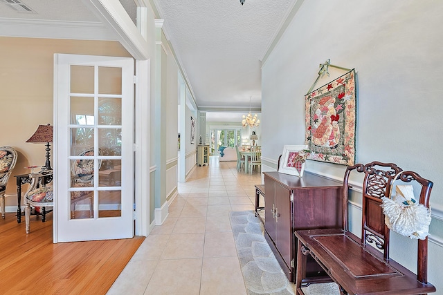 hall with a textured ceiling, a notable chandelier, crown molding, and light hardwood / wood-style flooring