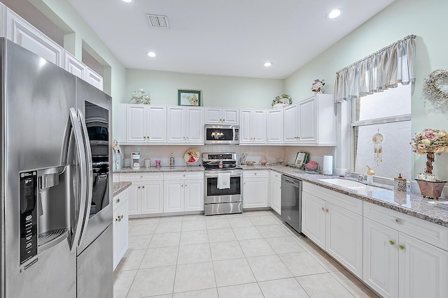 kitchen with white cabinets, sink, light tile patterned floors, light stone countertops, and appliances with stainless steel finishes