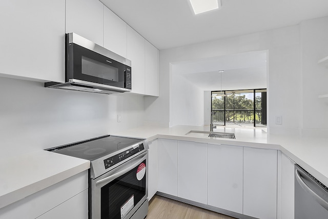 kitchen featuring kitchen peninsula, white cabinets, stainless steel appliances, and light hardwood / wood-style floors