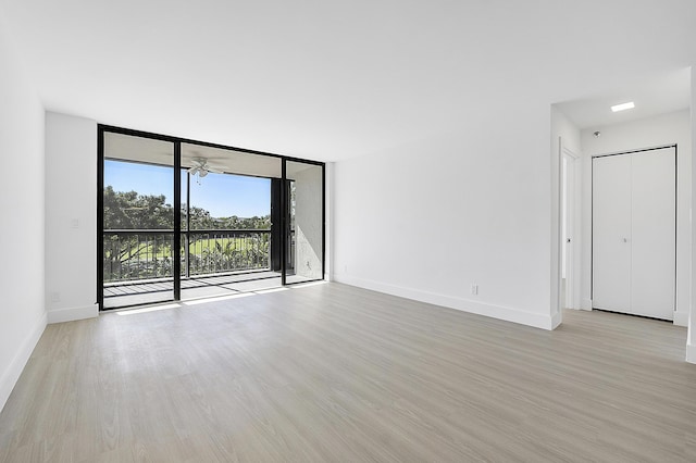 spare room with a wall of windows, ceiling fan, and light wood-type flooring