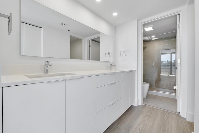 bathroom with wood-type flooring, vanity, toilet, and a shower with shower door