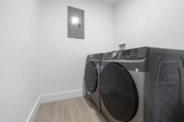 laundry room with electric panel, washer and clothes dryer, and light hardwood / wood-style flooring