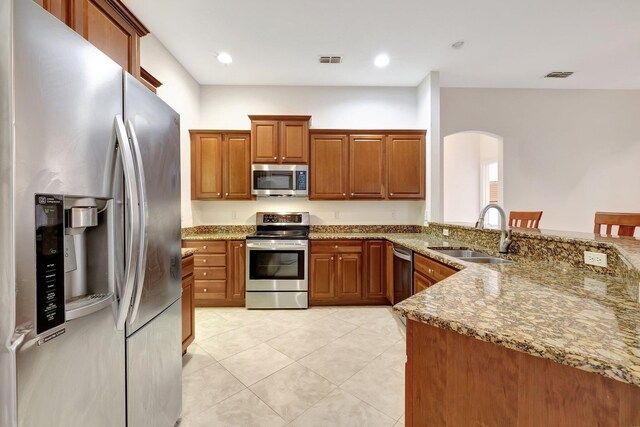 kitchen featuring kitchen peninsula, a kitchen bar, light stone countertops, stainless steel appliances, and sink