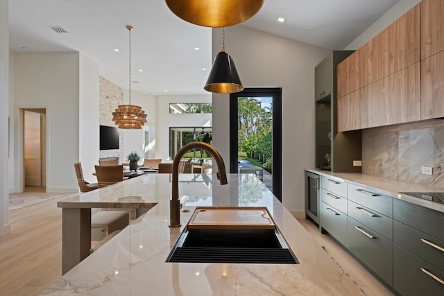 kitchen featuring sink, wine cooler, light stone counters, decorative light fixtures, and light wood-type flooring