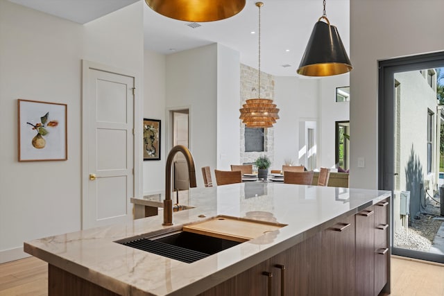 kitchen featuring a center island with sink, sink, hanging light fixtures, light hardwood / wood-style flooring, and light stone counters