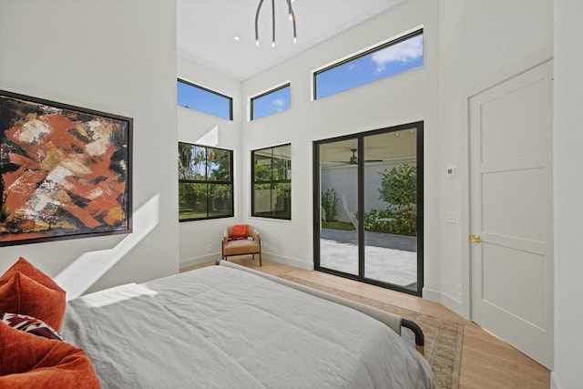 bedroom featuring a towering ceiling, access to outside, and light hardwood / wood-style flooring