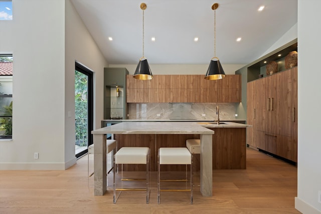 kitchen with decorative light fixtures, a kitchen island with sink, and light hardwood / wood-style flooring