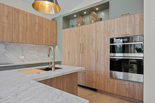 kitchen featuring sink, light stone counters, double oven, decorative backsplash, and light wood-type flooring