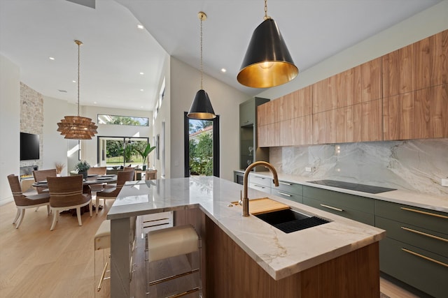 kitchen with sink, light stone counters, pendant lighting, a center island with sink, and light wood-type flooring