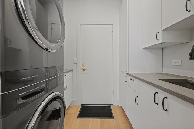 clothes washing area with stacked washing maching and dryer, sink, cabinets, and light hardwood / wood-style floors