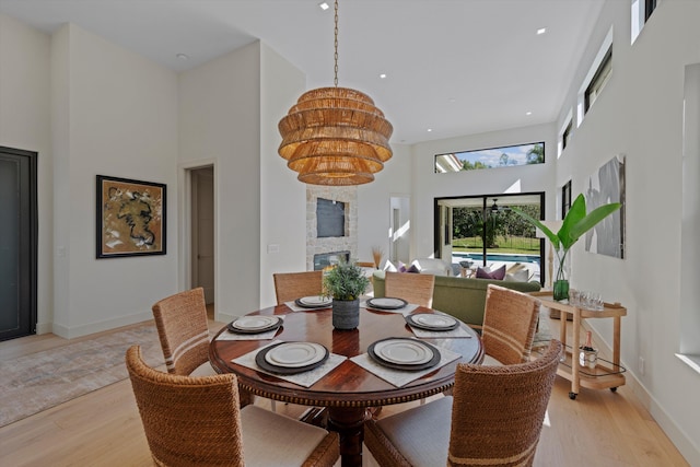 dining space featuring a stone fireplace, a towering ceiling, and light wood-type flooring