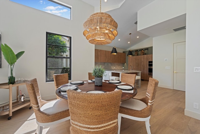 dining area with a chandelier, light hardwood / wood-style floors, high vaulted ceiling, and sink