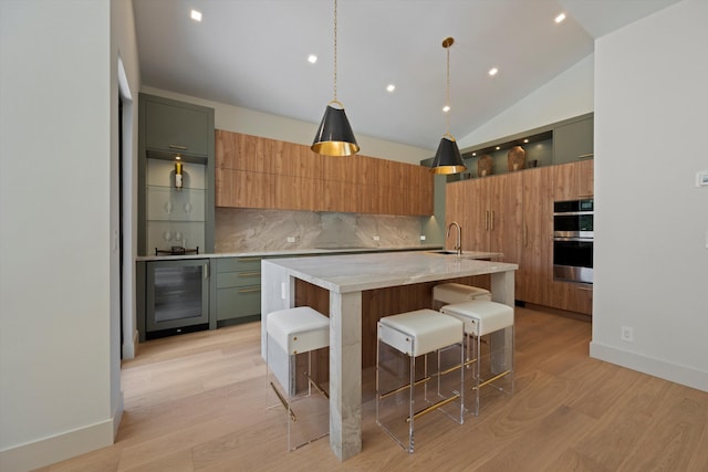 kitchen with lofted ceiling, a kitchen island with sink, wine cooler, decorative light fixtures, and light stone counters