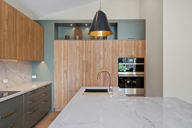 kitchen with sink, light stone counters, lofted ceiling, decorative light fixtures, and light wood-type flooring