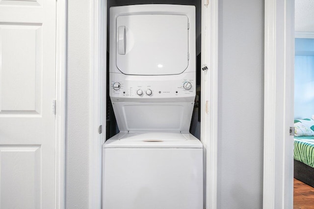 washroom with stacked washing maching and dryer and wood-type flooring