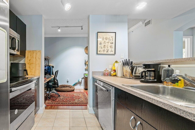 kitchen with sink, ornamental molding, a textured ceiling, appliances with stainless steel finishes, and light tile patterned flooring