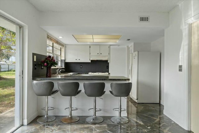 kitchen with visible vents, white cabinets, dark countertops, freestanding refrigerator, and a peninsula