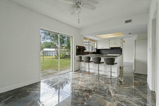 kitchen with marble finish floor, visible vents, freestanding refrigerator, white cabinetry, and a peninsula