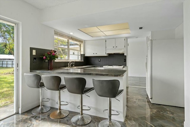 kitchen with white appliances, under cabinet range hood, white cabinetry, and marble finish floor