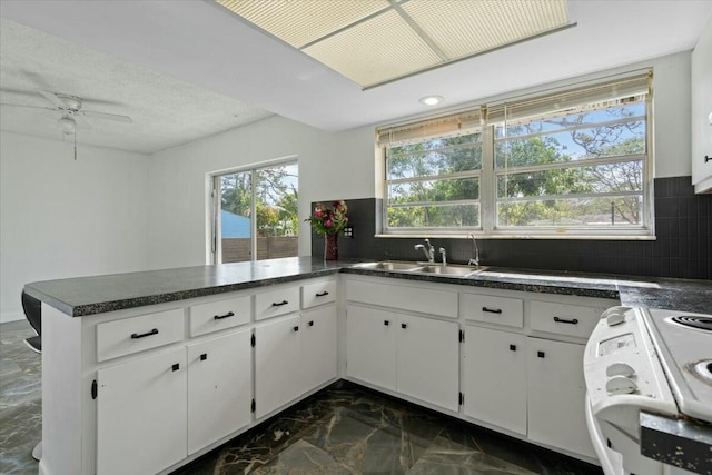 kitchen with dark countertops, white cabinetry, a sink, and a peninsula