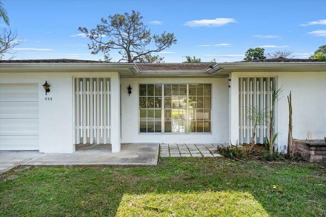 property entrance featuring a garage, a yard, and stucco siding