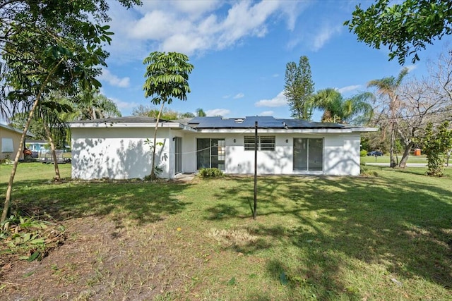 rear view of property featuring roof mounted solar panels and a lawn