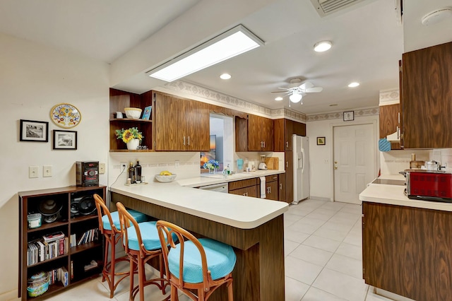 kitchen featuring ceiling fan, white fridge with ice dispenser, light tile patterned floors, tasteful backsplash, and kitchen peninsula