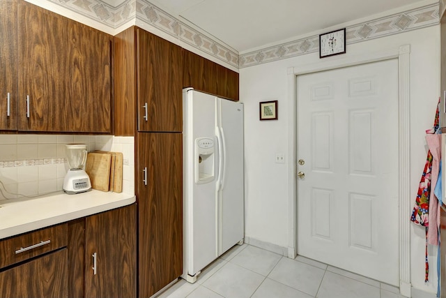 kitchen featuring backsplash, light tile patterned floors, and white refrigerator with ice dispenser