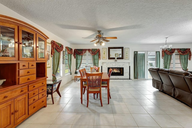 tiled dining space featuring a fireplace, plenty of natural light, ceiling fan with notable chandelier, and a textured ceiling