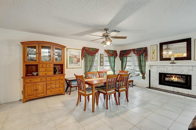 tiled dining area with ceiling fan, a textured ceiling, and a high end fireplace