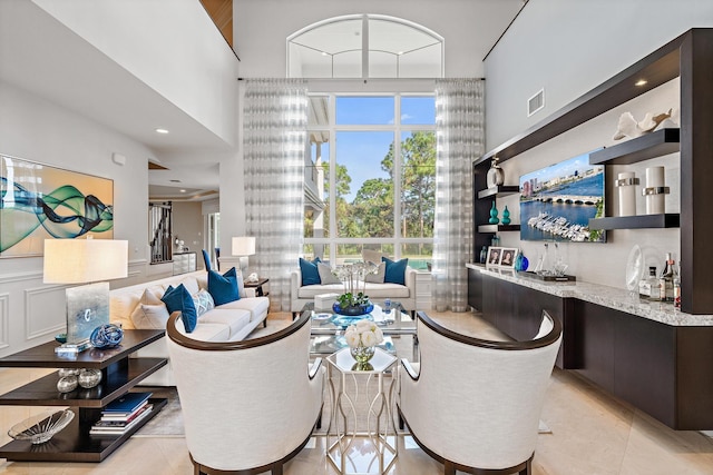 interior space featuring light tile patterned floors, a high ceiling, visible vents, and wet bar