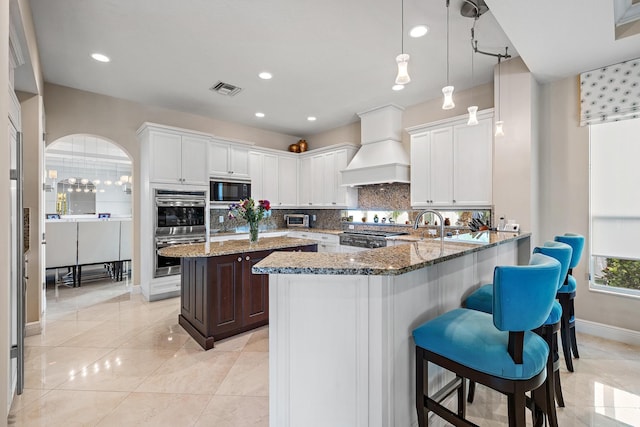 kitchen with black microwave, premium range hood, dark stone countertops, and visible vents