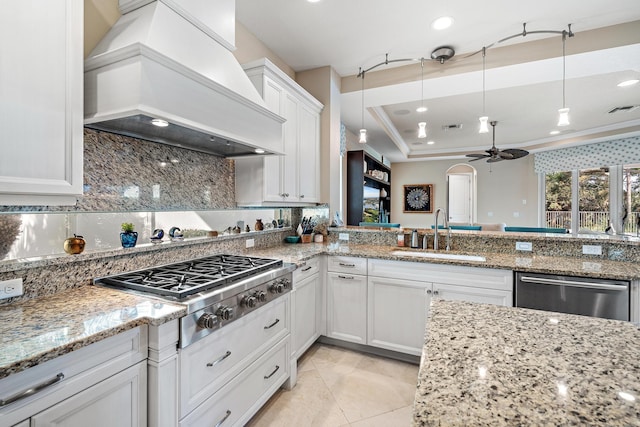 kitchen with white cabinets, appliances with stainless steel finishes, light stone countertops, premium range hood, and a sink