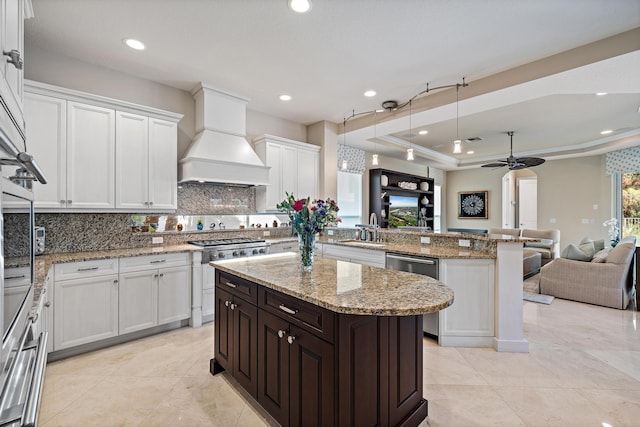 kitchen featuring a kitchen island, custom range hood, open floor plan, a tray ceiling, and a sink