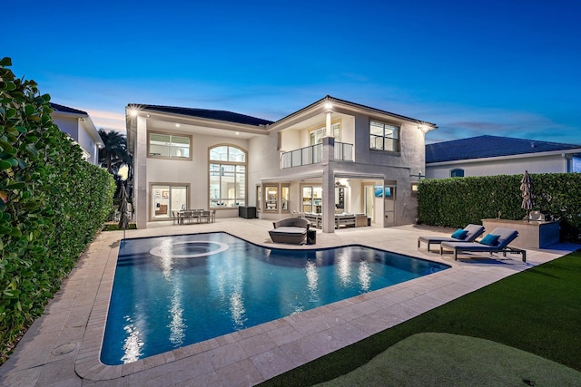 back of property at dusk with a patio, a balcony, an outdoor pool, french doors, and stucco siding