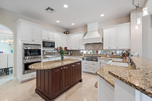 kitchen featuring stainless steel appliances, a peninsula, a sink, visible vents, and custom range hood