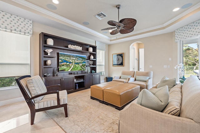 living area with arched walkways, a tray ceiling, ornamental molding, and visible vents