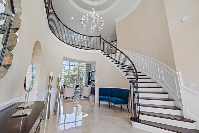 foyer entrance featuring marble finish floor, crown molding, a decorative wall, an inviting chandelier, and wainscoting