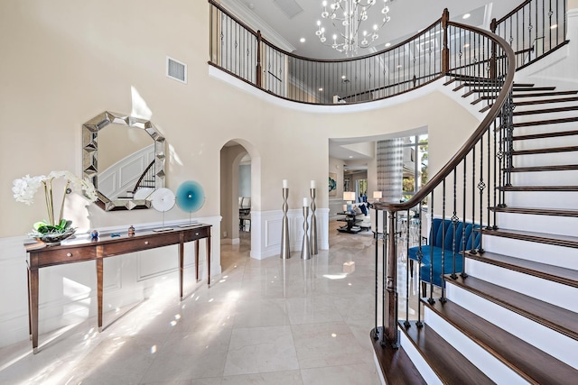 foyer entrance with visible vents, arched walkways, a wainscoted wall, a chandelier, and a decorative wall