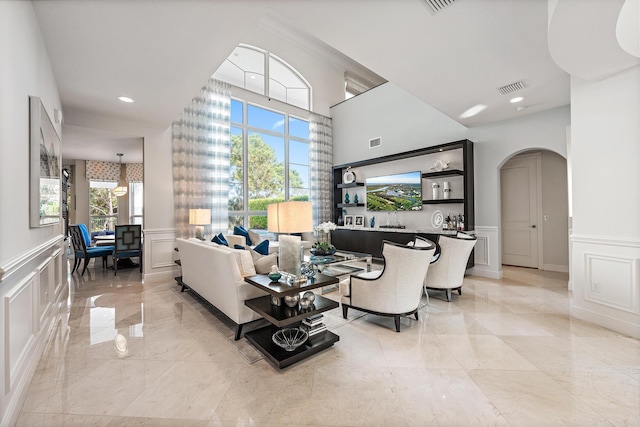 living area featuring visible vents, arched walkways, wainscoting, marble finish floor, and a decorative wall