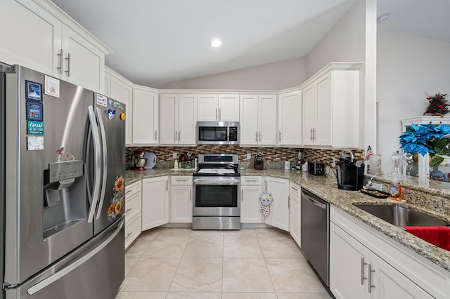 kitchen with light stone countertops, white cabinetry, stainless steel appliances, lofted ceiling, and light tile patterned floors