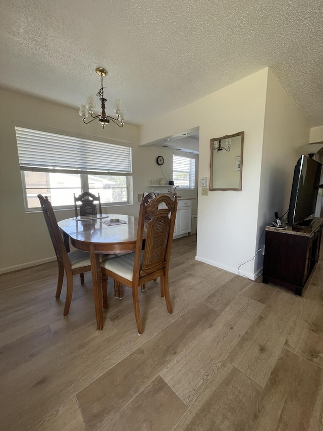 dining room with light wood-type flooring, a textured ceiling, and a chandelier