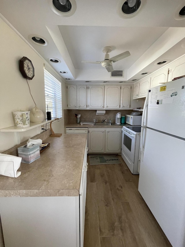 kitchen featuring white appliances, backsplash, dark wood-type flooring, a raised ceiling, and ceiling fan