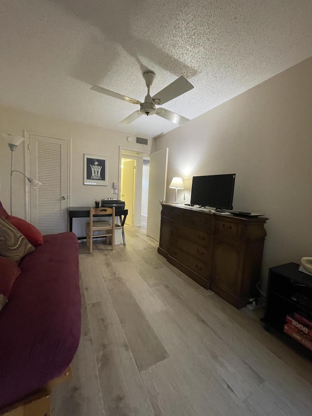 living room with ceiling fan, light hardwood / wood-style flooring, and a textured ceiling