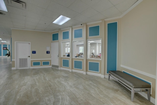 unfurnished living room with a drop ceiling and ornamental molding