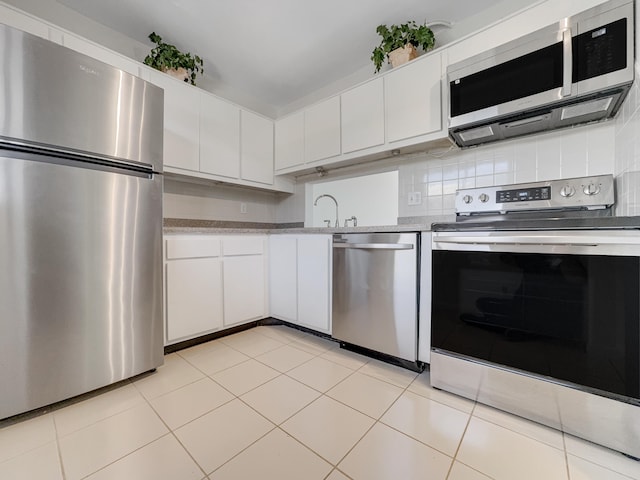 kitchen with appliances with stainless steel finishes, light tile patterned floors, white cabinetry, and backsplash