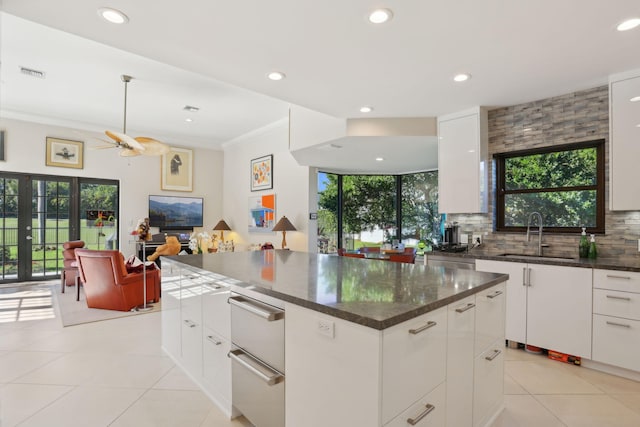 kitchen featuring white cabinets, a center island, crown molding, and sink