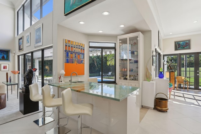 kitchen featuring a kitchen breakfast bar, french doors, crown molding, sink, and light tile patterned floors