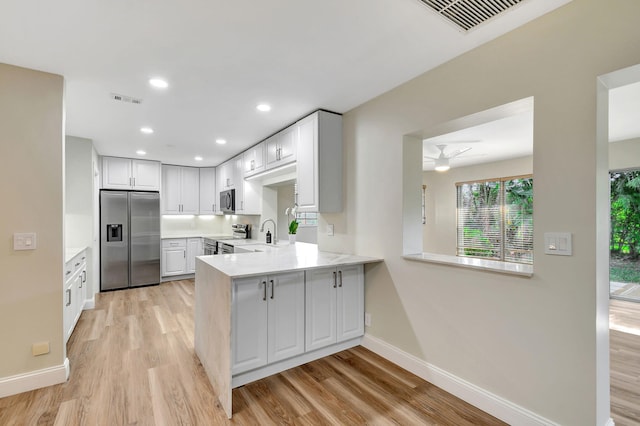 kitchen featuring appliances with stainless steel finishes, light hardwood / wood-style flooring, white cabinets, and kitchen peninsula